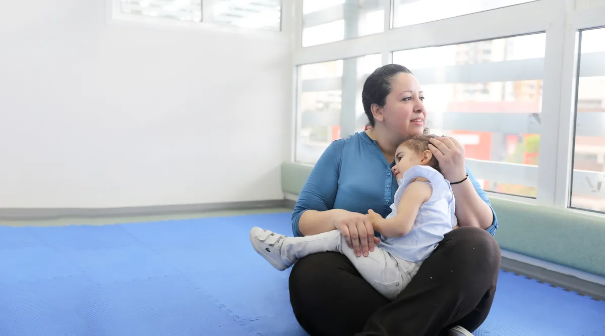 Caregiver cradling a sleepy infant on a soft blue play mat at L'académie des bébés