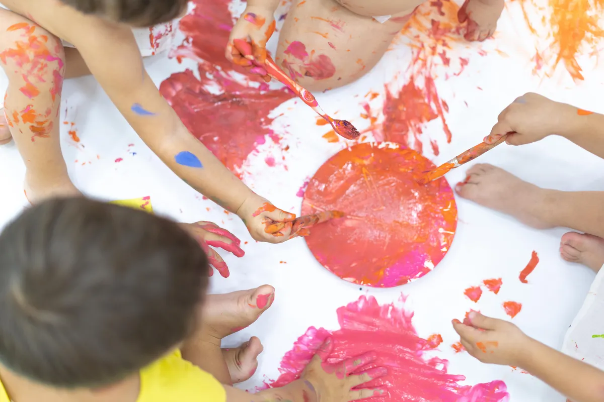 Toddlers finger-painting together with bright red and pink paint